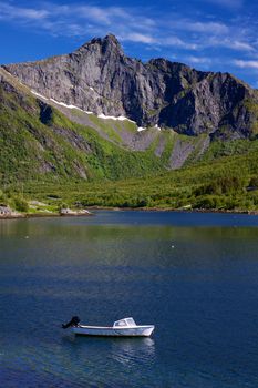 Small motor boat in fjord surrounded by towering mountains on Lofoten islands in Norway