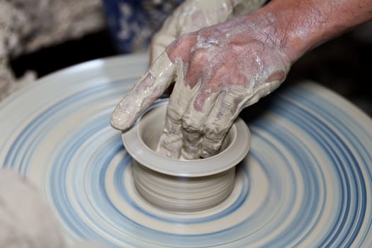 hands on a piece of pottery made of clay on a rotating wheel.