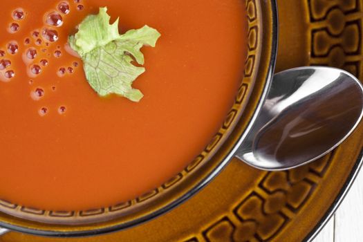 Tomato soup with green leaf garnish on a ceramic bowl