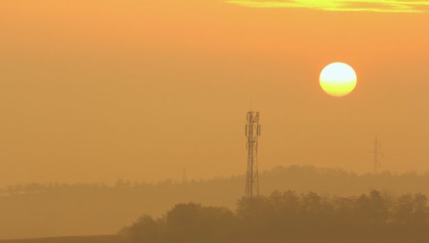 Sun rising over the mist in a wild area. Environmental damage made by man placing telecommunication antennas.