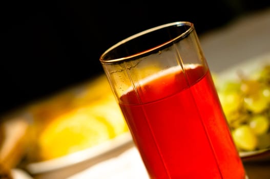 Red fruit-drink in glass in still life composition with orange and grape