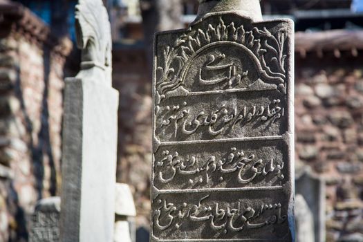 Close up photo of a gravestone with islamic writing on it  in a cemetery of a mosque on a sunny day
