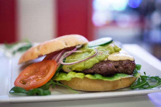 An open hamburger sandwich on a plate showing the patty meat, the tomato, lettuce, mayo and onion