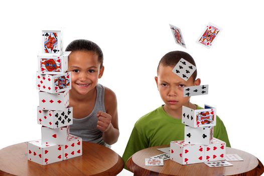 A young girl smiles happily when she wins a card building competition against her brother, whose tower collapses.