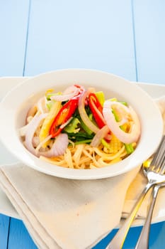 spicy vegetarian noodle in a white plate and light blue wooden table