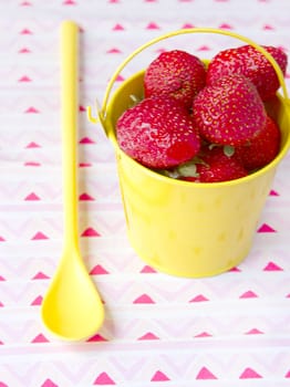 Yellow small bucket with strawberries and yellow spoon next