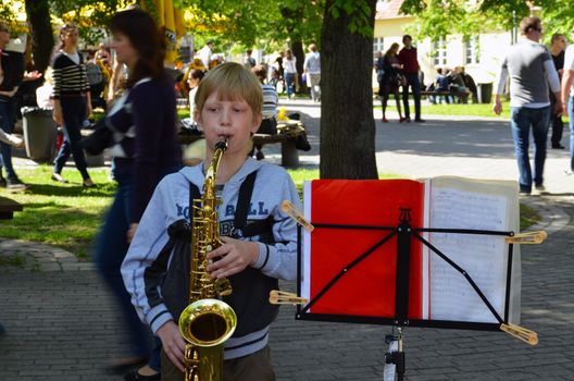 VILNIUS, LITHUANIA - MAY 2012 - Unidentified child play saxophone. People walk around. Street Musician Day.