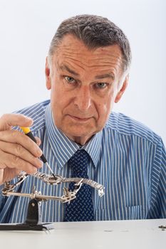An older man wearing a shirt and tie, repairing a watch.