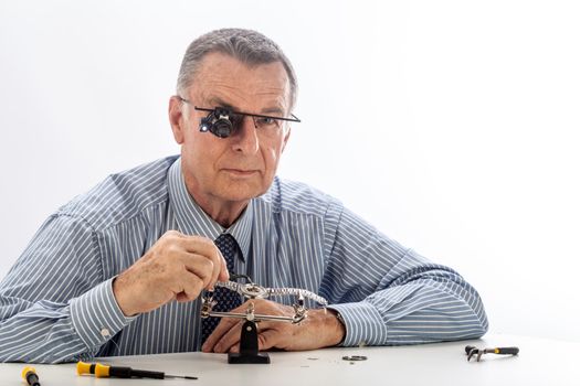 An older man wearing a shirt and tie, repairing a watch.