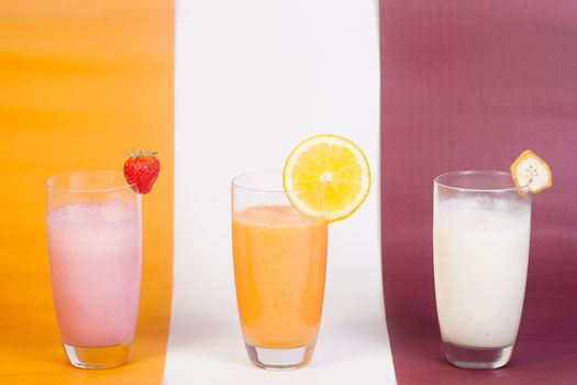 3 different juices and vitamins (strawberry, orange and banana) isolated on a color background.