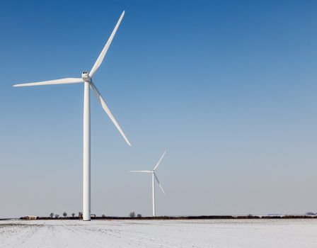 Two windturbines on a field covered by snow in winter.