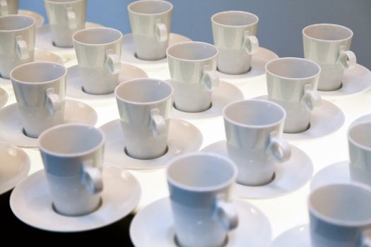Many white coffee mugs in a line over a buffet
