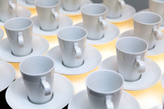 Many white coffee mugs in a line over a buffet