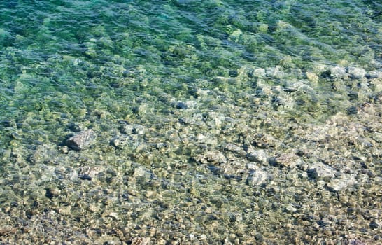 Abstract of shallow crystal clear blue water of Aegean Sea in a beach in Bodrum, Turkey, with pebbles, suitable for use as a background.