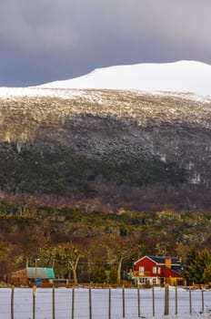 A farmhouse with a snowy hill and forest behind it.