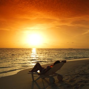 Woman in chaise-lounge relaxing on sunset beach