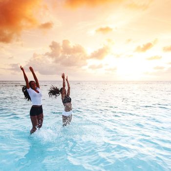 Two happy wimen playing in water on sunset