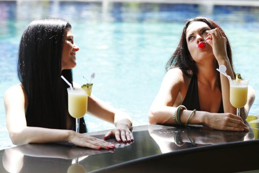 Two beautiful women relaxing in swimming pool with cocktails