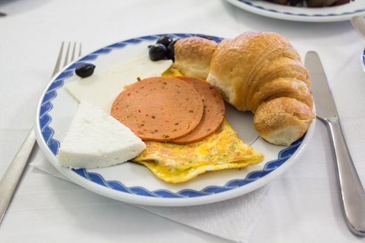 A hearty breakfast with several slices of ham, cheese, eggs and croissant