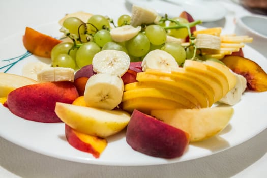 A plate filled with ripe and tasty peaches, banana and grapes