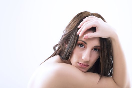 Serious pensive attractive woman with bare shoulders and tousled long brunette hair looking directly at the camera in studio