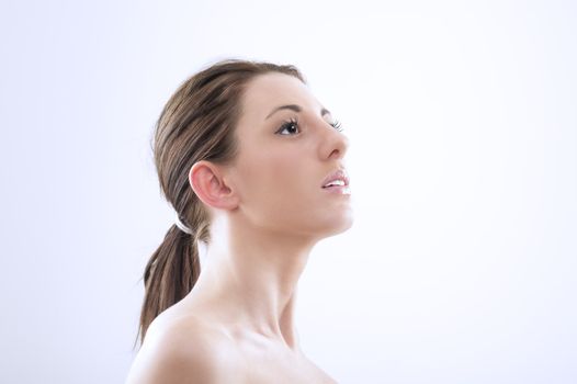 Beautiful graceful woman witth bare shoulders craning her neck and looking upwards, head and shoulder portrait