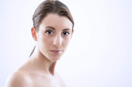 Head and shoulders studio portrait of a beautiful sexy woman with bare shoulders, a natural complexion and her hair tied back in a ponytail looking at the camera with large lustrous eyes