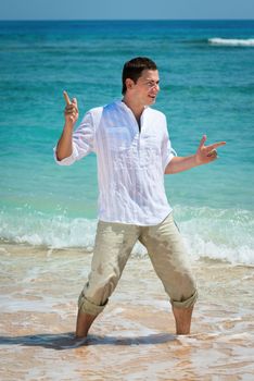 Happy young man dancing at the tropical beach in blue sea water