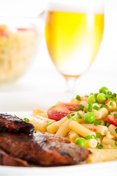 Steak and pasta salad with a glass of beer in background
