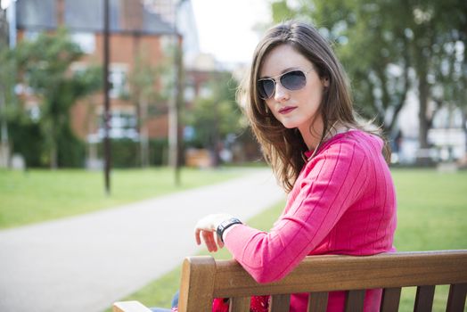 Portrait of beautiful young woman sitting on bench in park