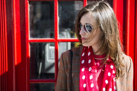 Portrait of beautiful young woman wearing sun glasses and leaning against London red phone booth