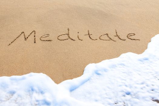 Meditate - written in the sand with a foamy wave underneath