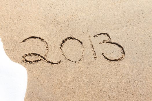 2013 written in the sand on a beach with foamy water about to wash it away.