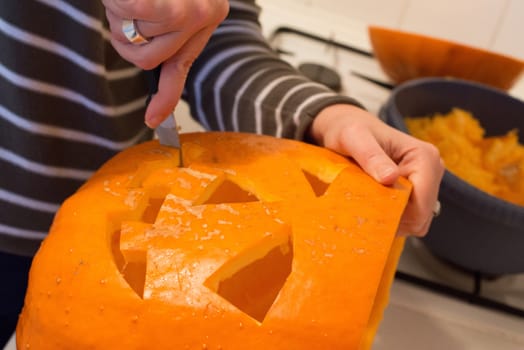 Halloween jack o lantern preparation - woman carving a pumpkin with a knife