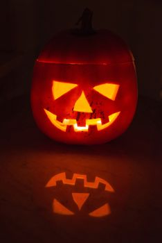 Glowing halloween pumpkin with scary face with great reflection on marble