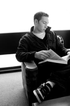 A young college aged man reading a book at the library in black and white.