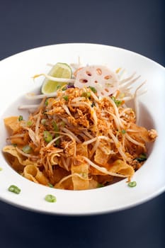 A Thai dish of crispy noodles and bean sprouts in a large white bowl with chop sticks.