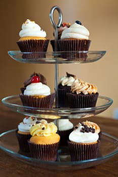 Tiered party serving tray with some decadent gourmet cupcakes frosted in a variety of flavors.