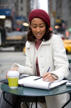 An African American business woman working in the city outdoors writes something down in her notepad.
