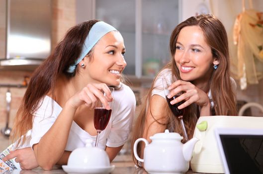 Happy women with glasses of red wine talk about on kitchen