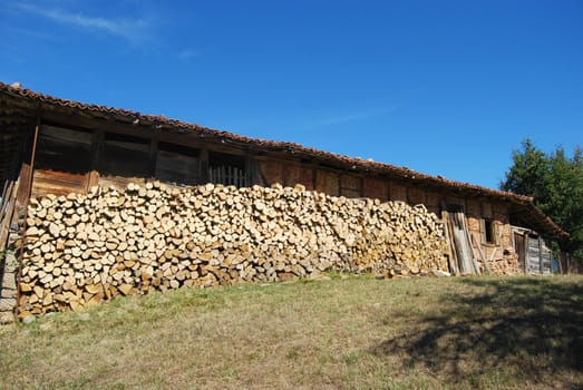 Old country wooden house stacked firewood, meadow, blue sky