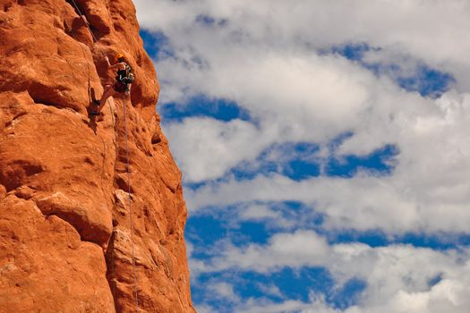 Extreme climber on red rock against blue sky and white clouds