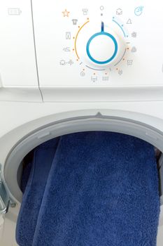 Open washing machine with control panel dial and blue  towel