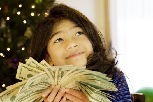 Little girl holding up large amount of cash at Christmas, daydreaming