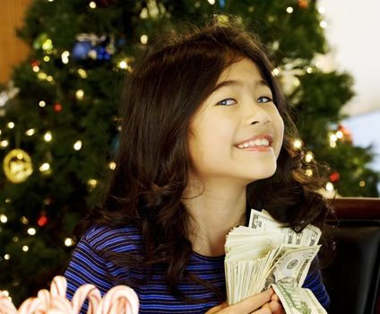 Little girl holding large amount of cash with Christmas tree in background