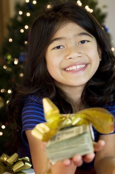 Little girl holding large amount of cash with Christmas tree in background
