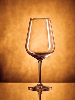 Empty elegant wine glass on yellow-brown background