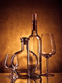 Empty cognac bottle,  cognac glass, wine bottle and wine glass on a reflective suface against grunge background