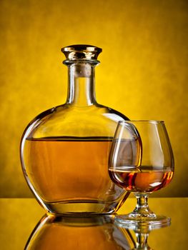 Round elegant bottle of cognac with a filled glass on yellow background