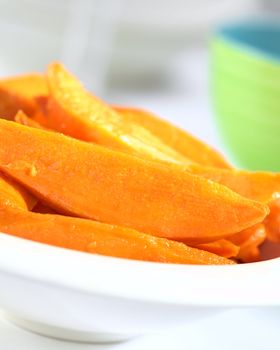 Fresh homemade caramelized sweet potato wedges in white bowl (Selective Focus, Focus one third into the sweet potatoes)